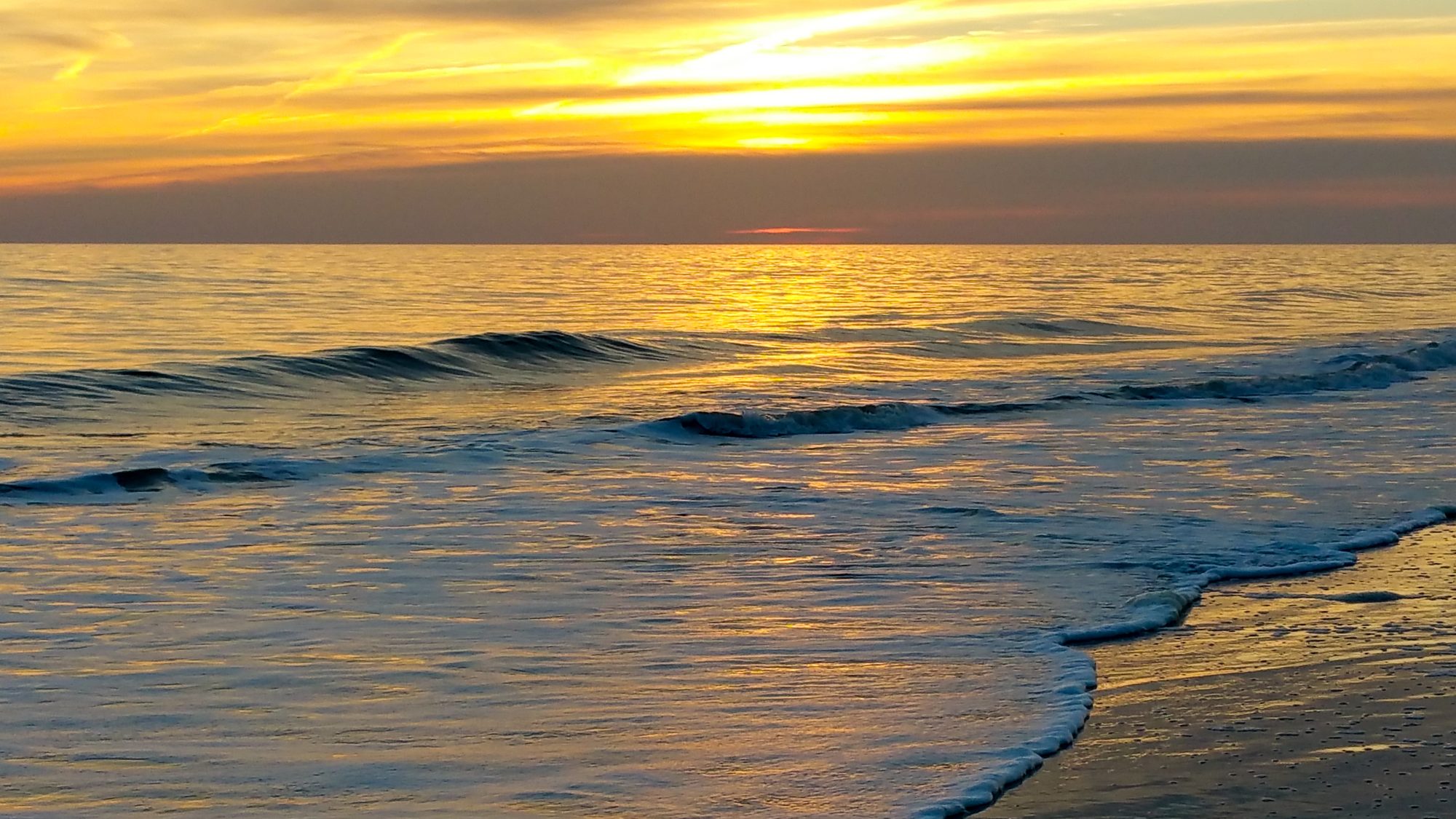 Luz dorada de la mañana sobre las olas en la playa de Oak Island