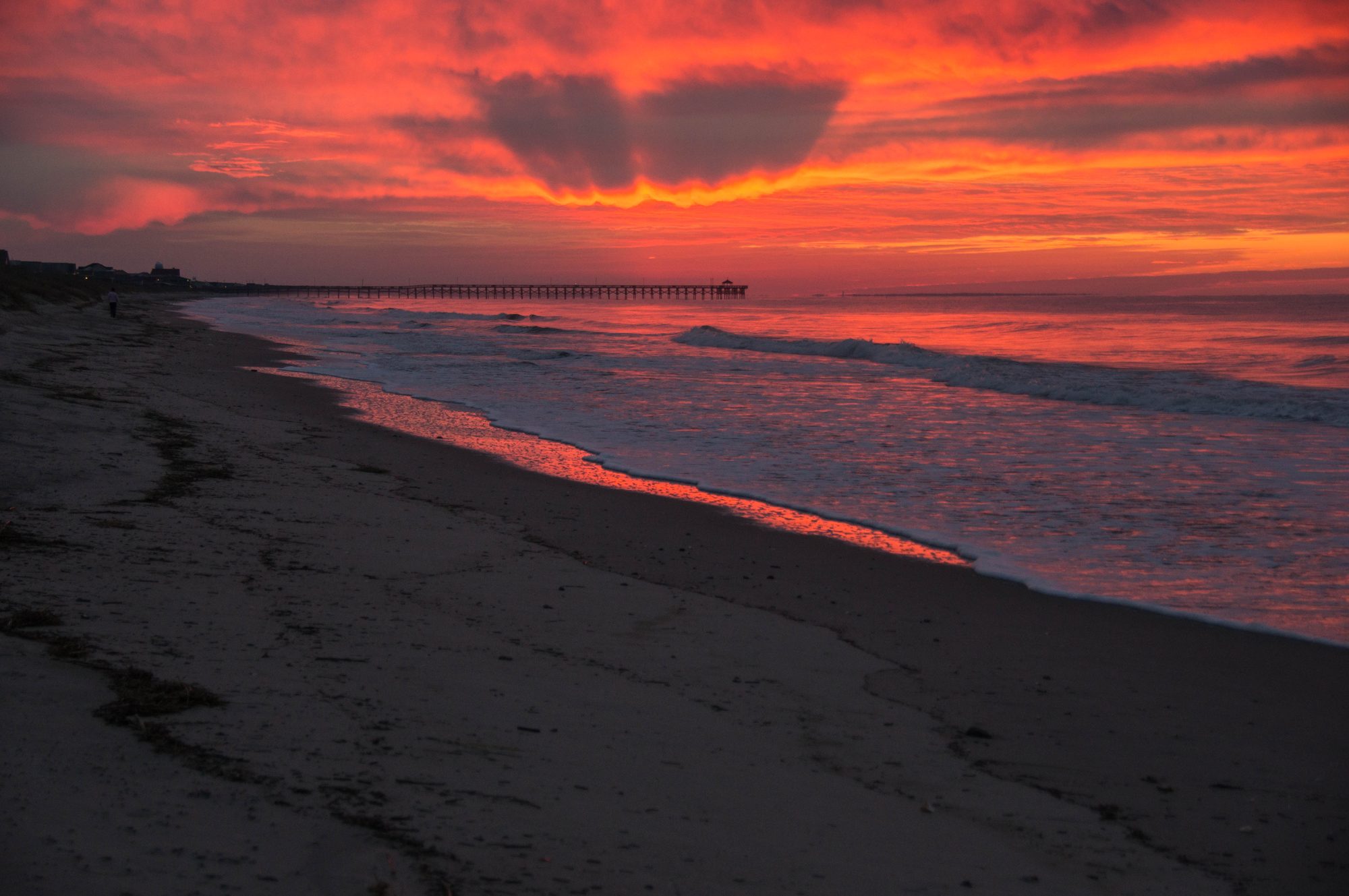 A red winter sunrise over the surf, looking down the beach toward the Ocean Crest Pier on Oak Island